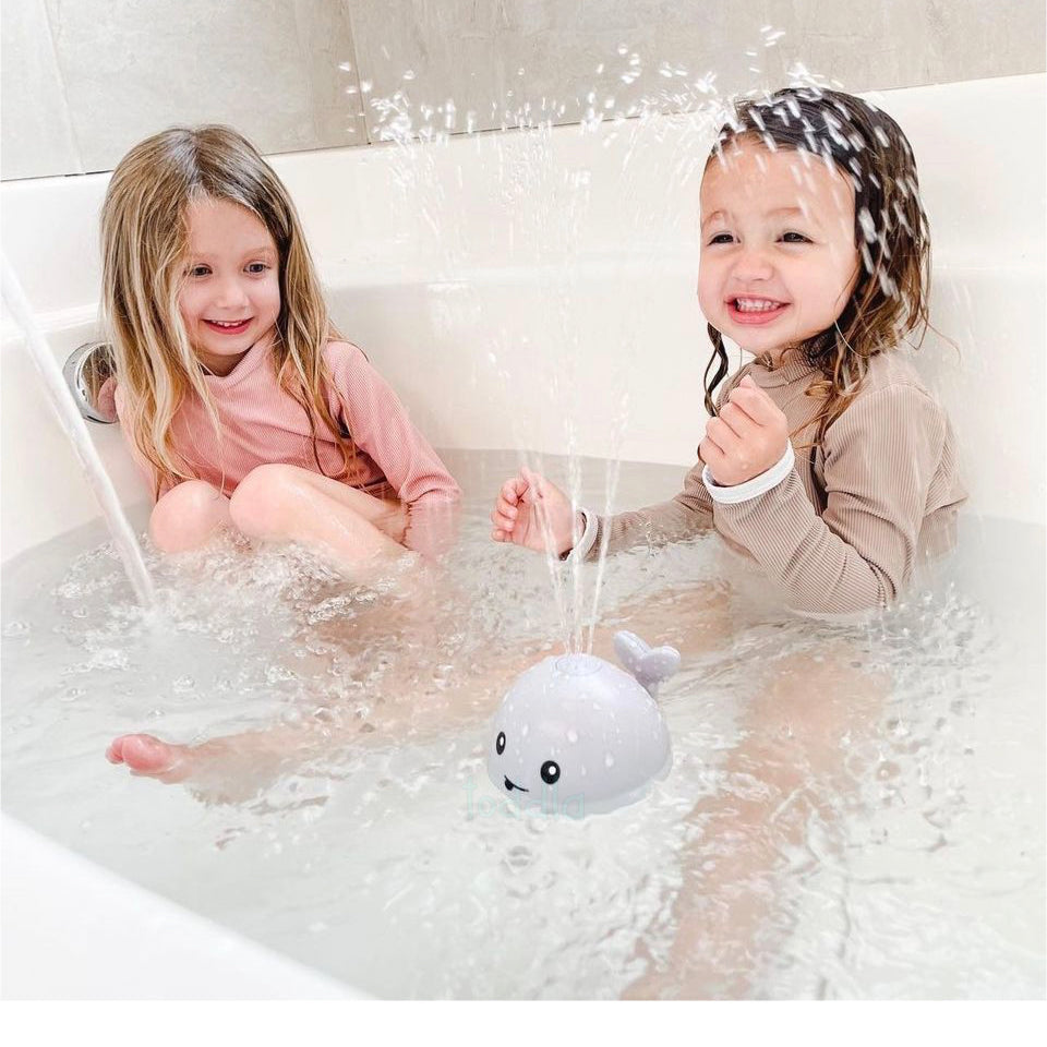 Two children in a bathtub with a toy whale, surrounded by bubbles.