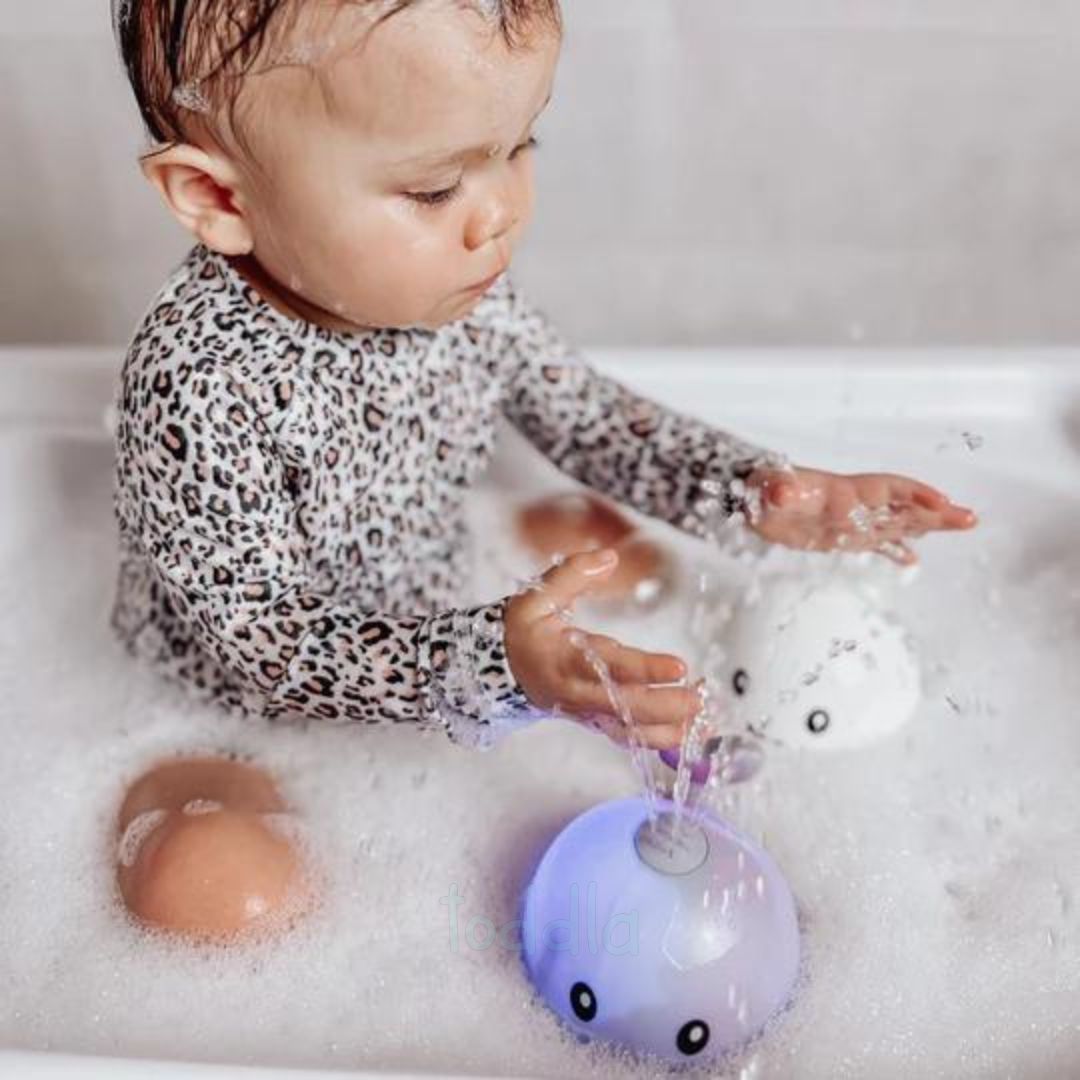 Baby playing with a bath toy in a bathtub filled with bubbles
