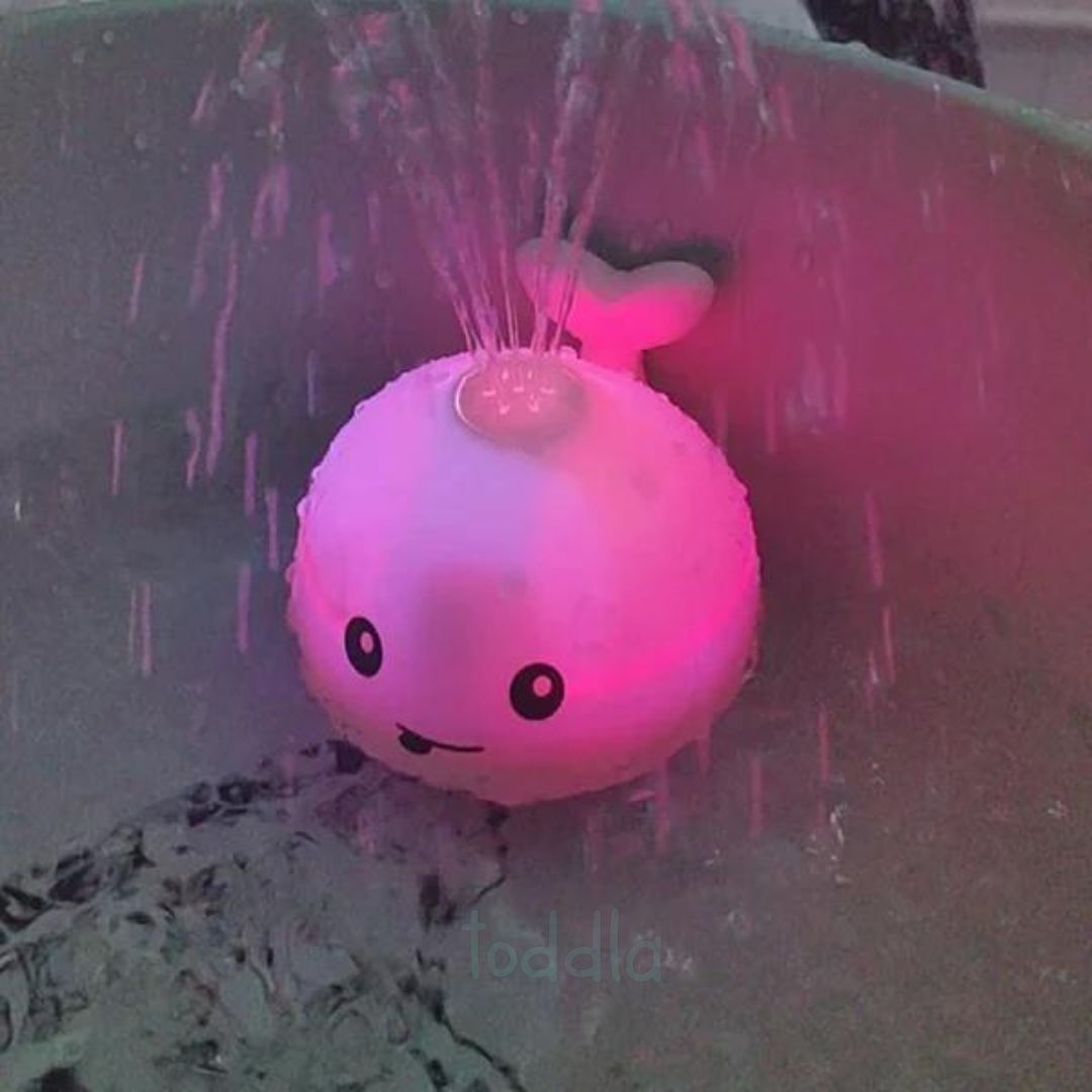 Pink and white toy whale with water splashing around it