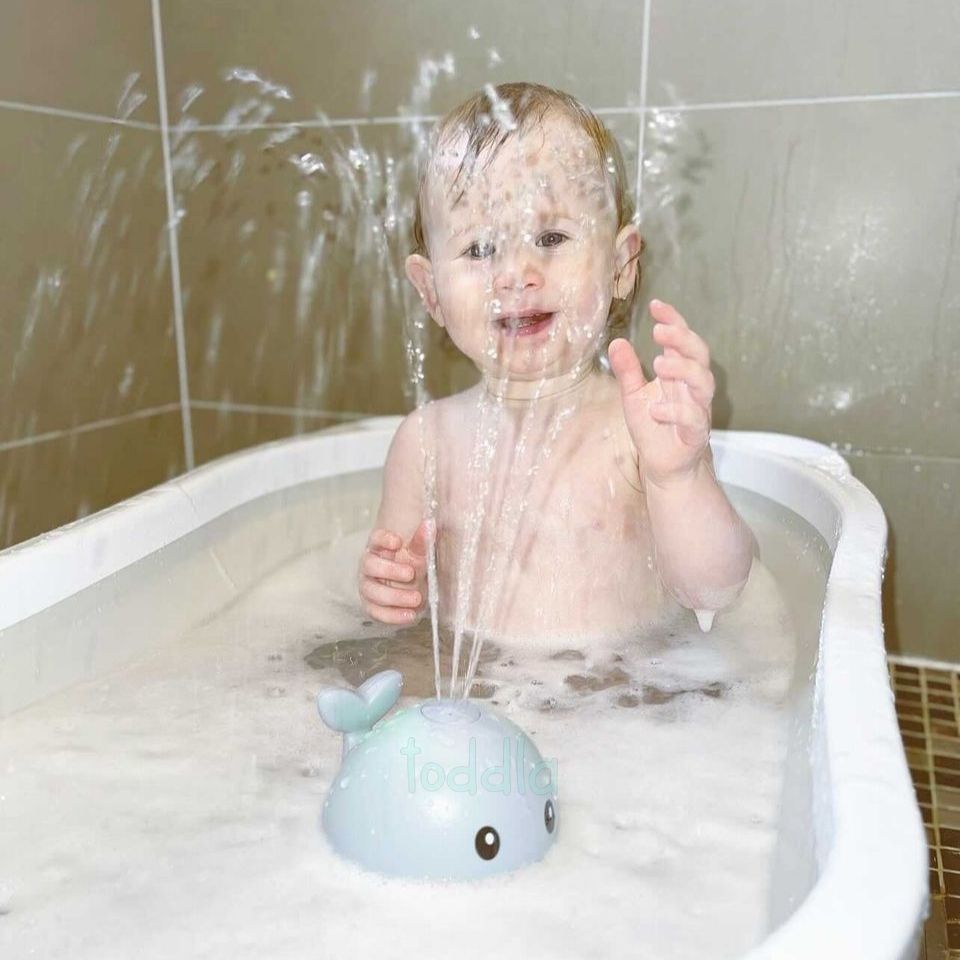 Child playing in a bathtub with a toy whale, water splashing around.