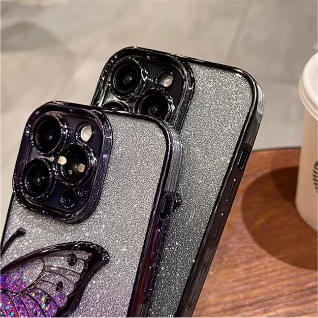Two phone cases with glittery finish and butterfly design on a wooden surface.