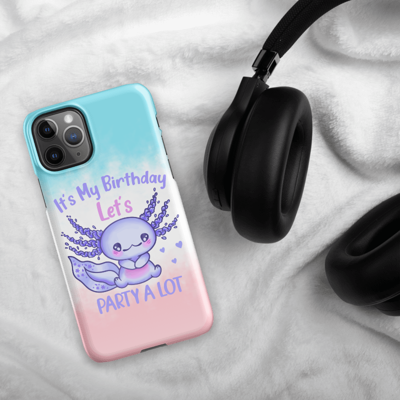Phone case with a cute purple creature design and text on a gradient background, placed on a textured surface with headphones.