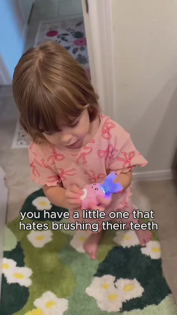 Young girl demonstrating the dinosaur kids electric toothbrush and smiling while brushing to show that brushing can be fun for children